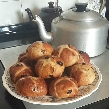 Photo of home made hot cross buns on a plate by the kettle and tea pots