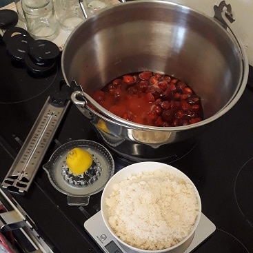 Picture of strawberries in a jam pan with sugar, lemon, thermometer and jars