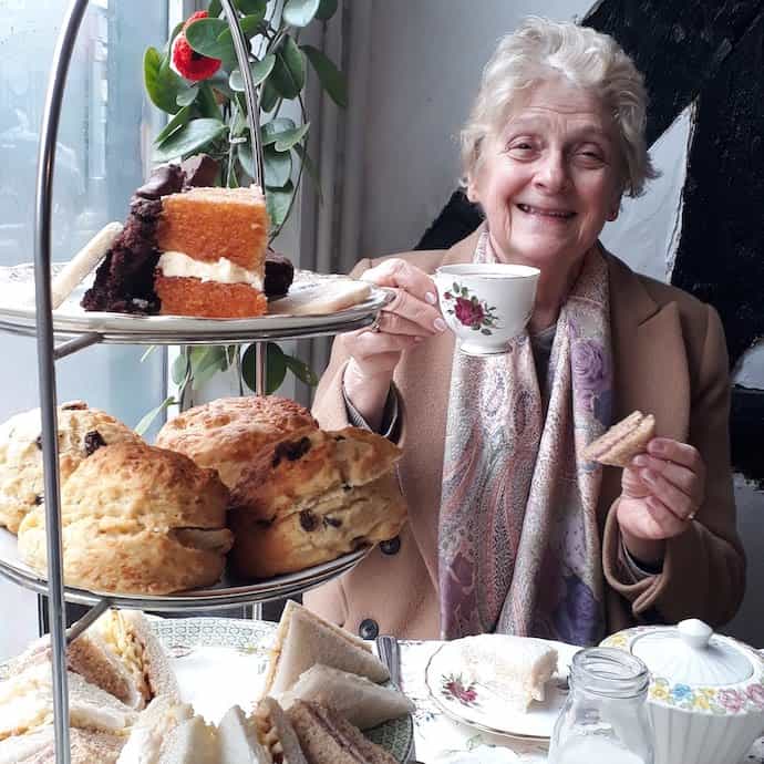 Picture of my mother enjoying afternoon tea for less, with a cake stand piled with scones, sandwiches and cakes